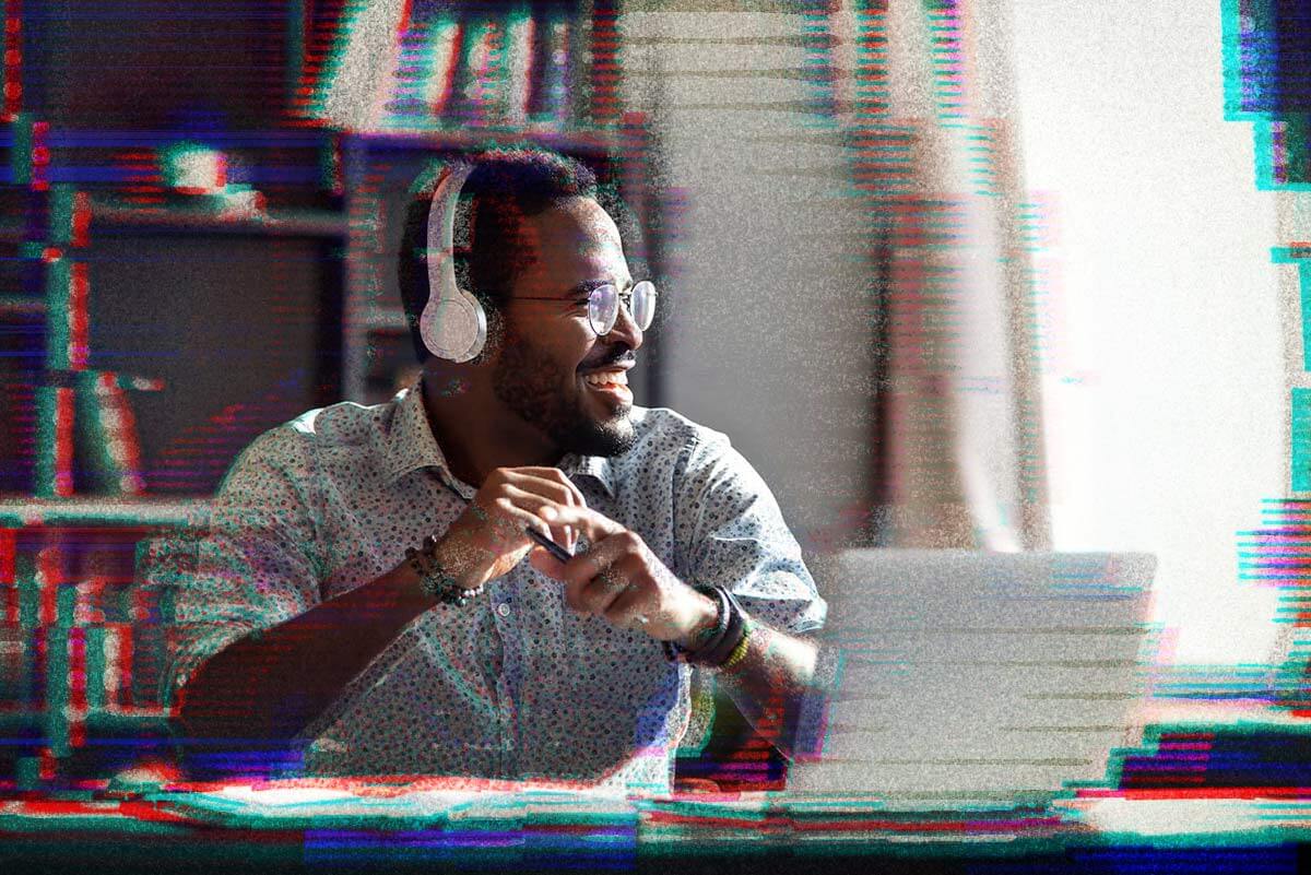 Black man with glasses and headphones smiling at desk with laptop
