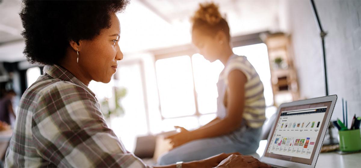 Black mother and daughter sitting at desk working on laptop