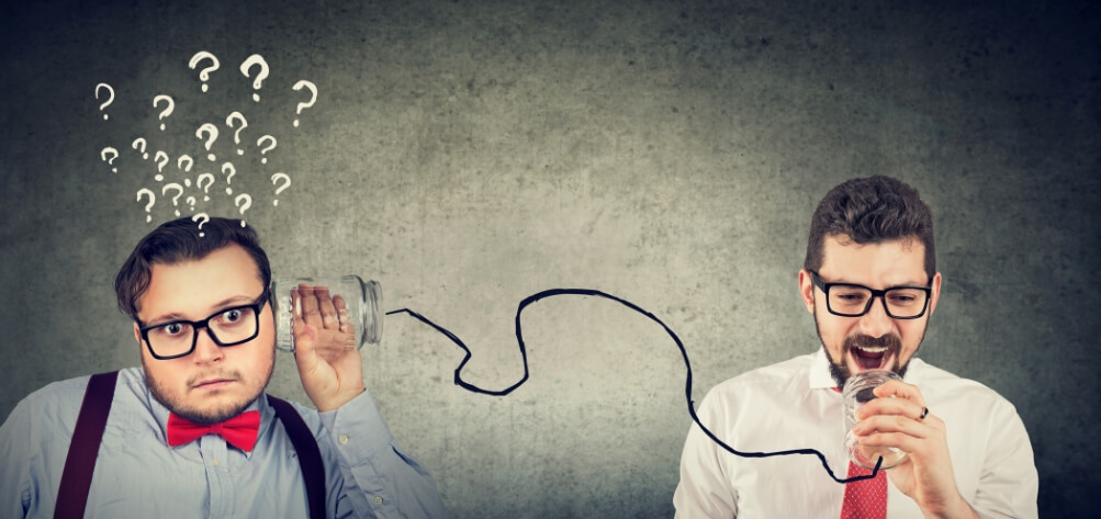 Communication concept. One business ment is speaking into a glass jar with a wire attached to another being held up to his colleagues ear. Illustrative question marks above the business man who is listening.