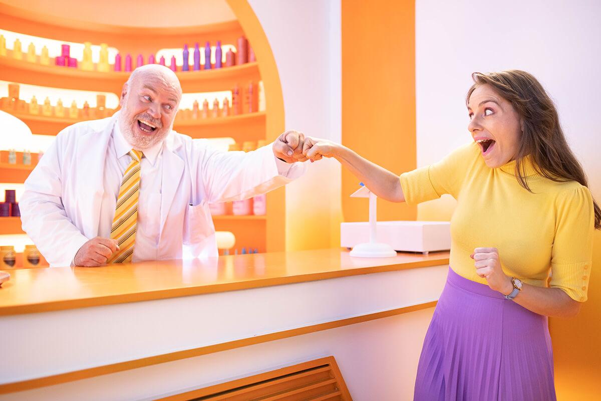 Woman and pharmacist fist bumping over counter in colorful pharmacy