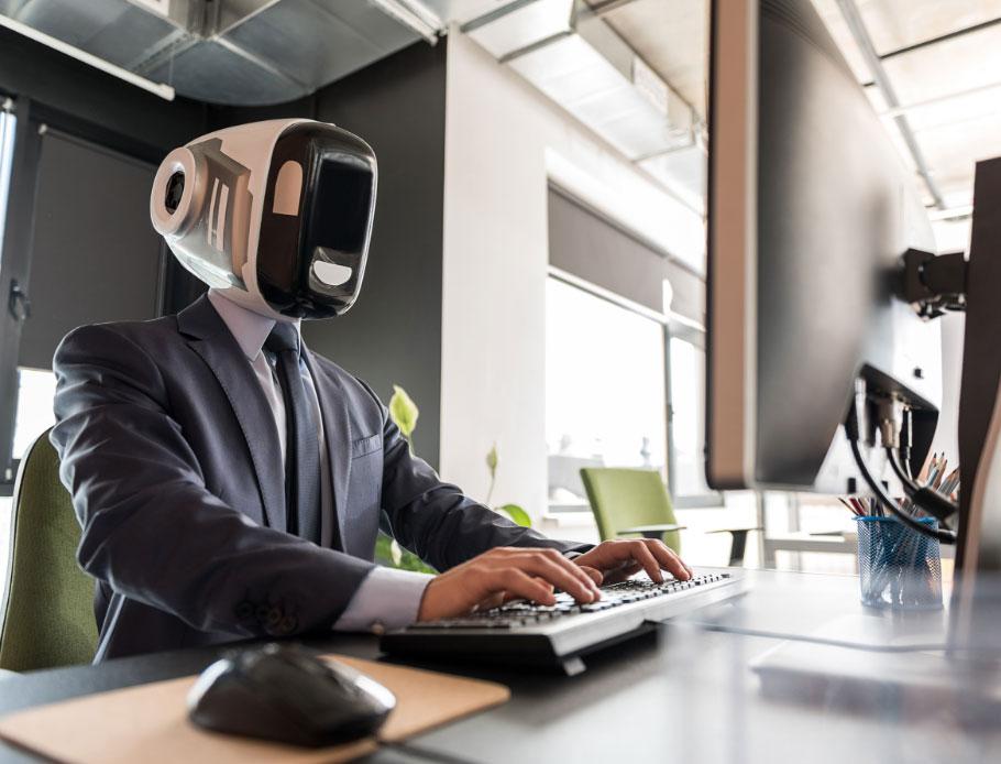 Robot with human hands sitting and typing on desktop monitor