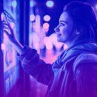 Blue and purple duotone image of a young woman interacting with a digital out of home advertisement outside in urban environment at night