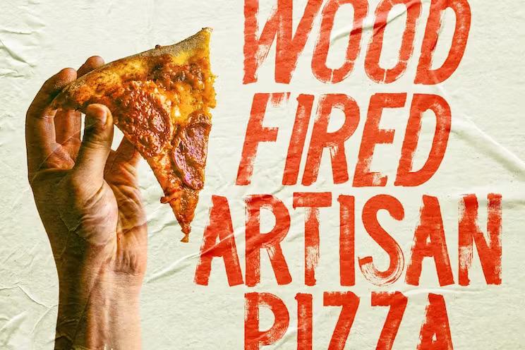 Hand holding a piece of wood fired artisan pizza