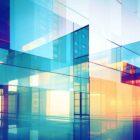 Abstract digital artwork of geometric glass structures in vibrant blue, orange, and pink hues, reflecting and refracting light to create a modern, futuristic cityscape effect.