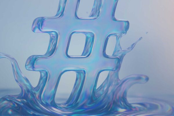 A translucent blue hashtag symbol rises from a swirling splash of liquid, with soft light creating a reflective, iridescent effect on the surface.