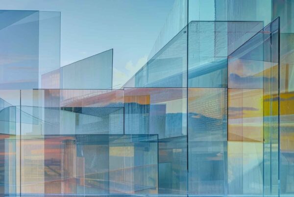 Abstract image of overlapping transparent geometric shapes in blue, yellow, and orange tones evokes modern glass buildings reflecting a cloudy sky—perfect for in-between days advertising with its fresh, contemporary appeal.