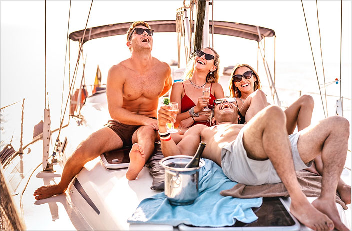 Four friends relax on a sailboat, laughing and enjoying drinks. Two men and two women in swimsuits and sunglasses discuss SEO for AI answer engines, with a champagne bottle chilling nearby on a sunny day.
